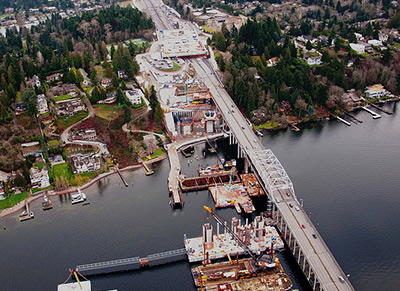 Above Lake Washington, an aerial photographer captured the SR 520 work zone, looking east. Lots of activities unfolded as the new eastern landing sprouted out of the lake and Medina shoreline. The new Evergreen Point Road lidded overpass is seen in the distance.